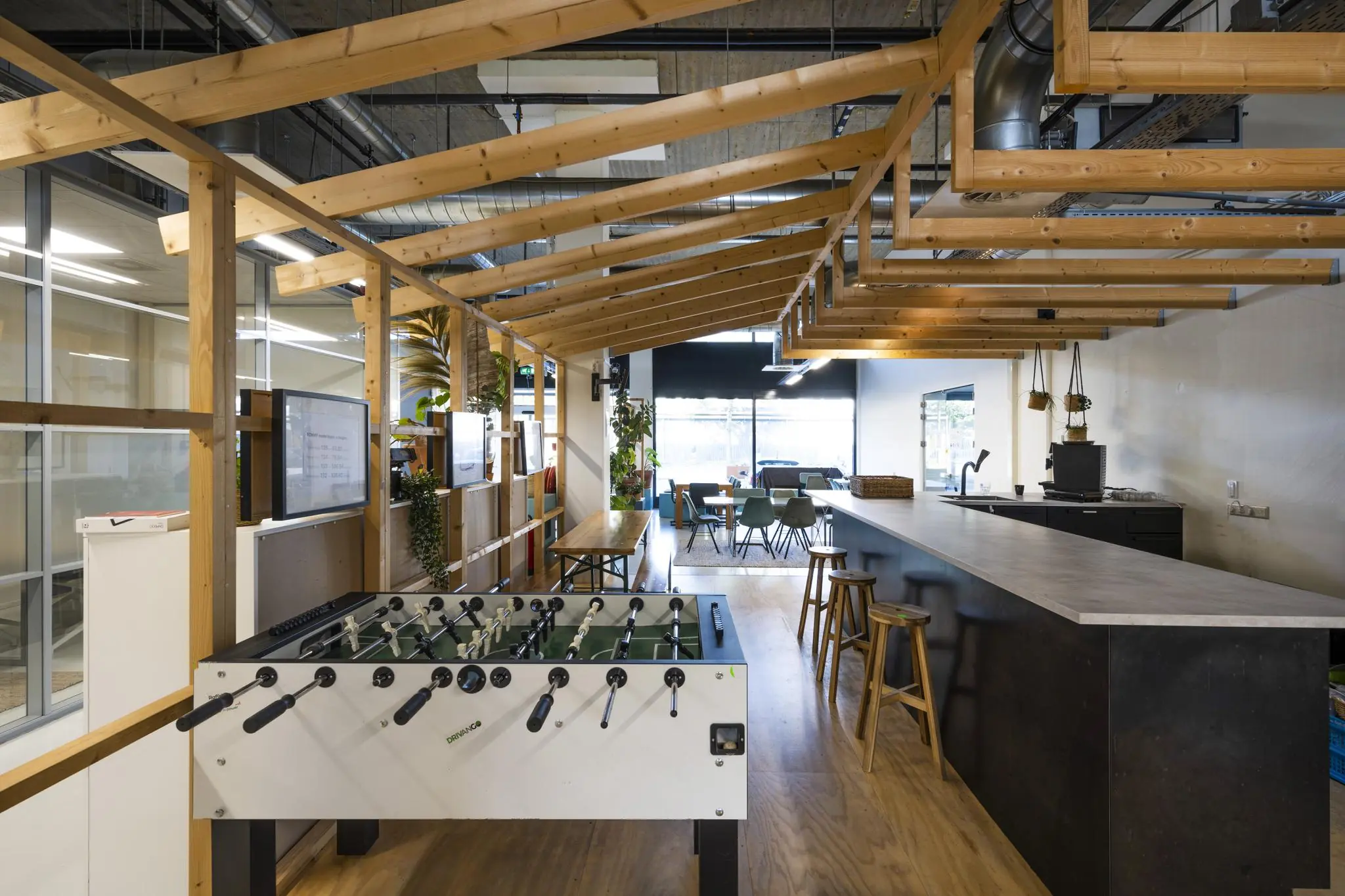 Moderne kantoorlounge aan de Joan Muyskenweg met een tafelvoetbaltafel, bar en zithoek onder een houten dakconstructie.